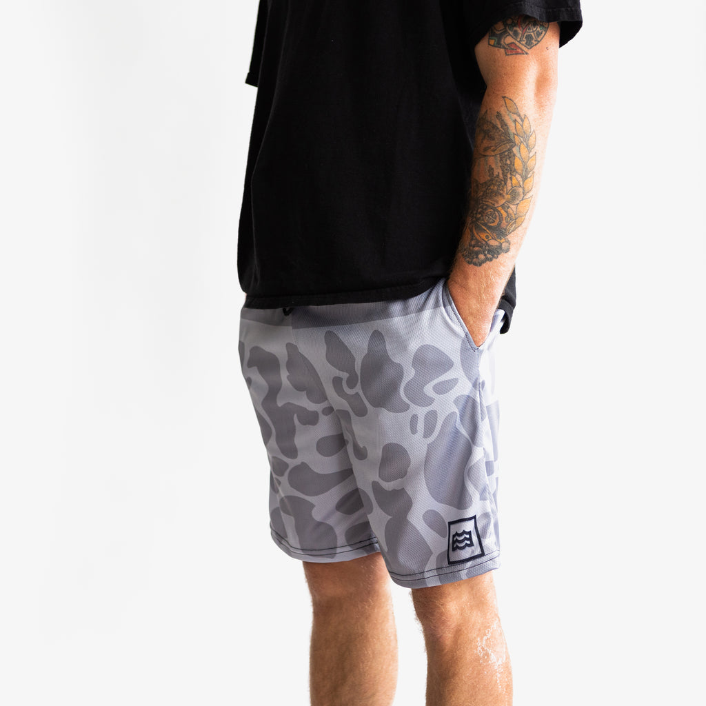 lower half of man with hands in pocket and wearing split white and gray camouflaged shorts