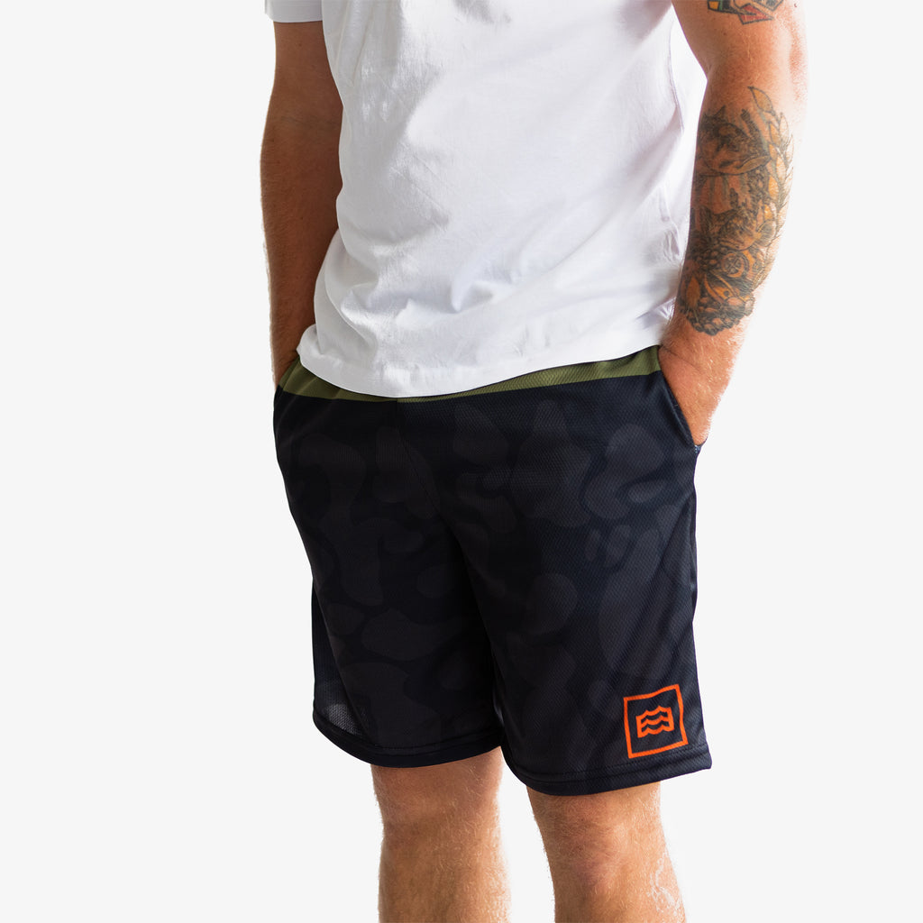 lower half of man with hands in pockets wearing split green and navy camouflaged shorts